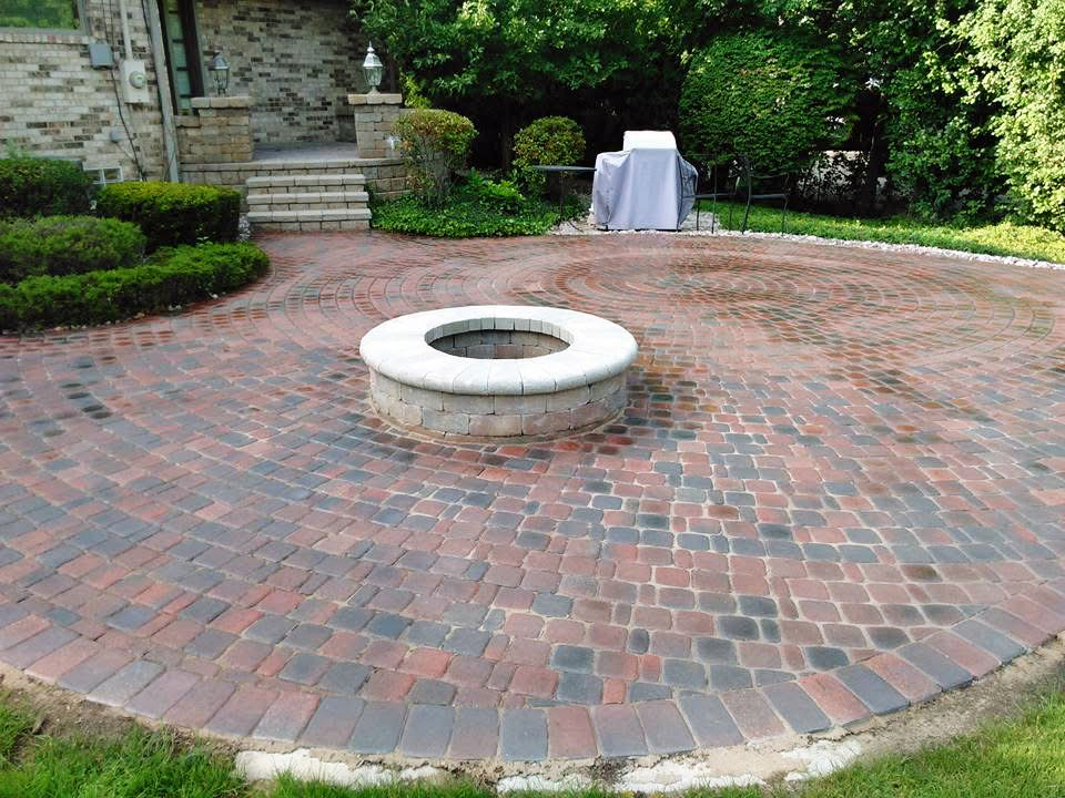 heritage landscape Custom hardscape design and installation featuring a circular brick paver patio, fire pit, and professional masonry work.