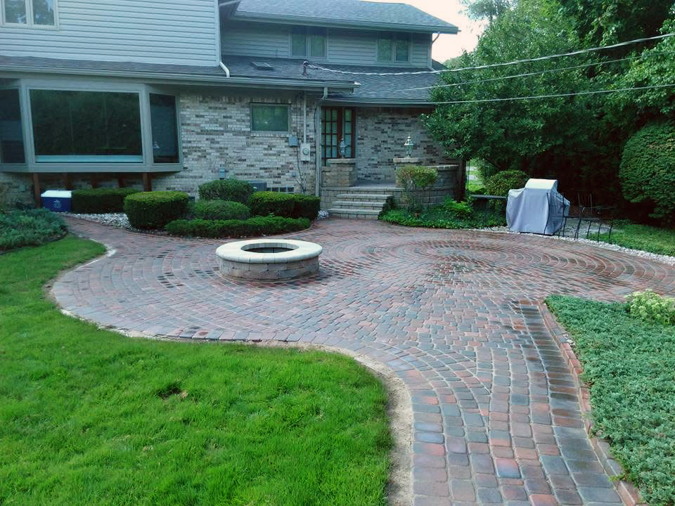 heritage landscape Custom hardscape design and installation featuring a circular brick paver patio, fire pit, and professional masonry work.