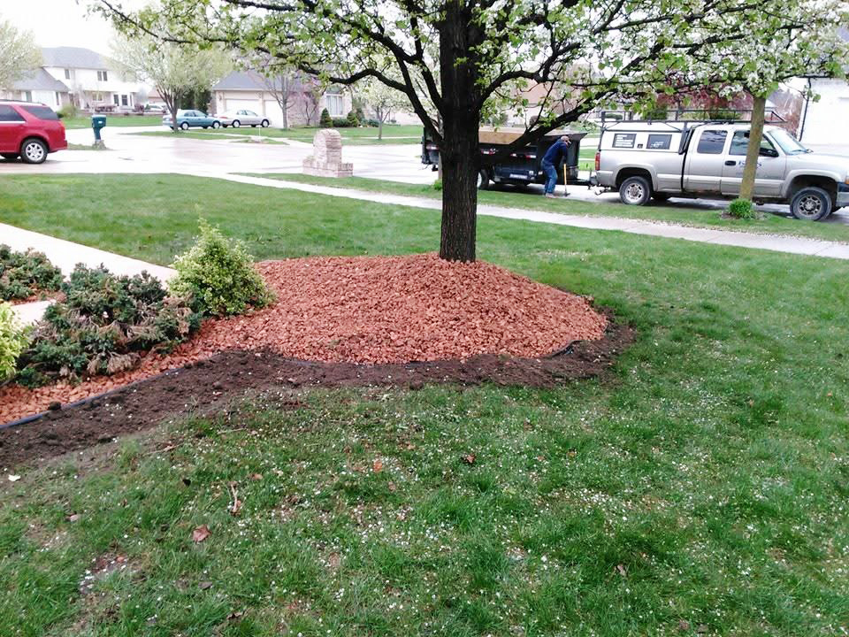 Heritage Landscape Professional landscaping service featuring garden bed edging, red mulch installation, and tree maintenance.