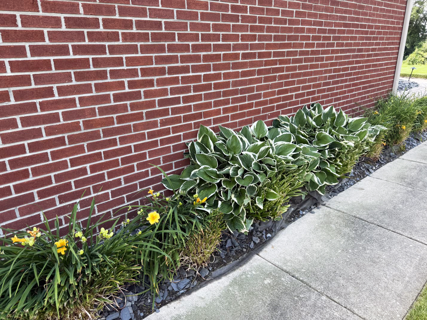 Heritage Landscape Professional landscape maintenance featuring plant bed installation and stone mulch along a brick exterior