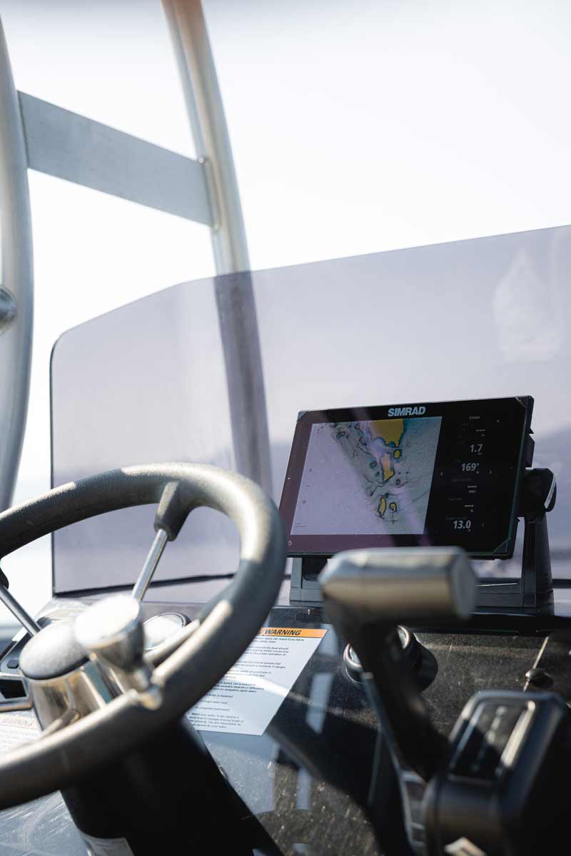 Boat steering wheel and throttle controls with a Simrad navigation screen displaying a marine chart.