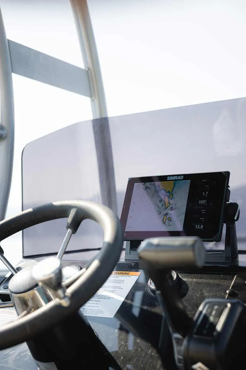 Boat steering wheel and throttle controls with a Simrad navigation screen displaying a marine chart.