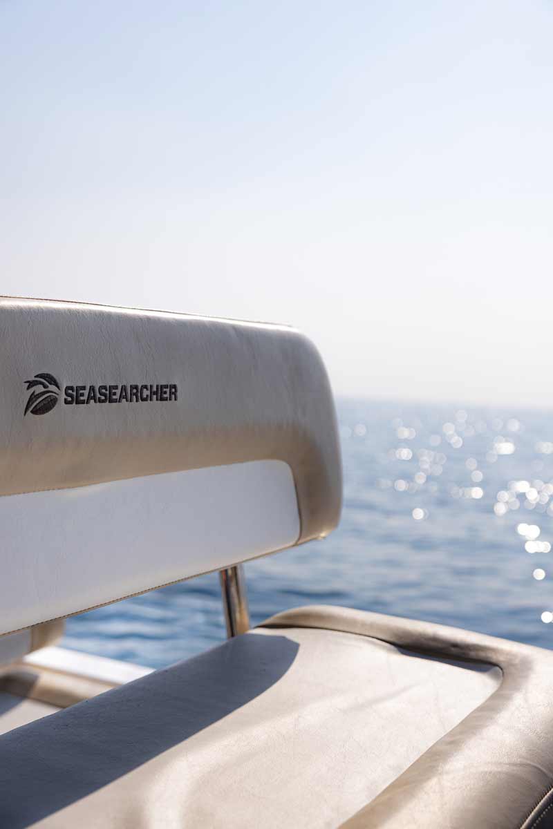 Beige boat seat with SEASEARCHER logo, overlooking a sparkling blue sea under a clear sky.