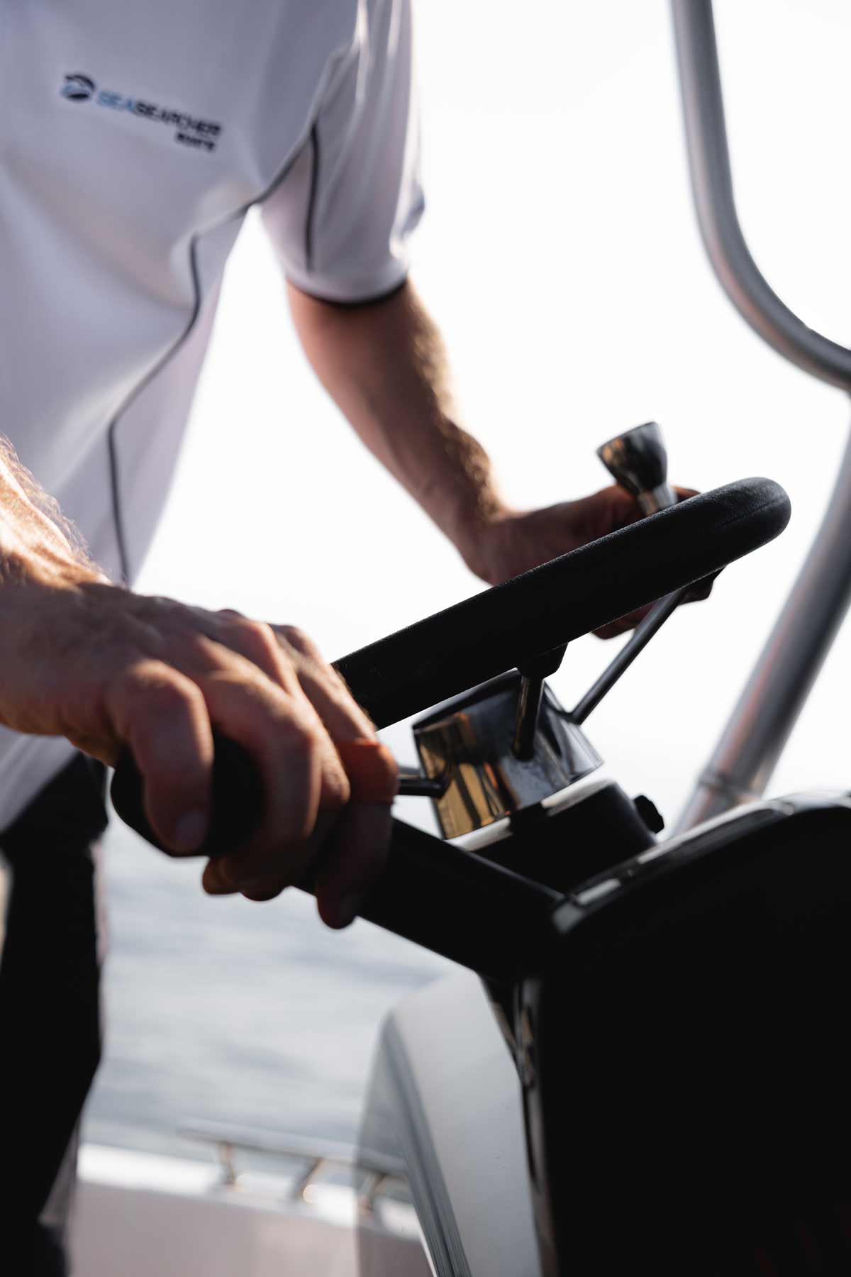 Person steering a boat with hands on the wheel and throttle control, wearing a Seasearcher shirt.