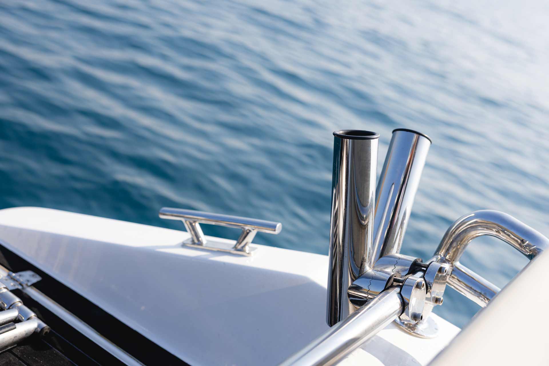 Close-up of stainless steel fishing rod holders mounted on the edge of a white boat deck with calm water in the background.