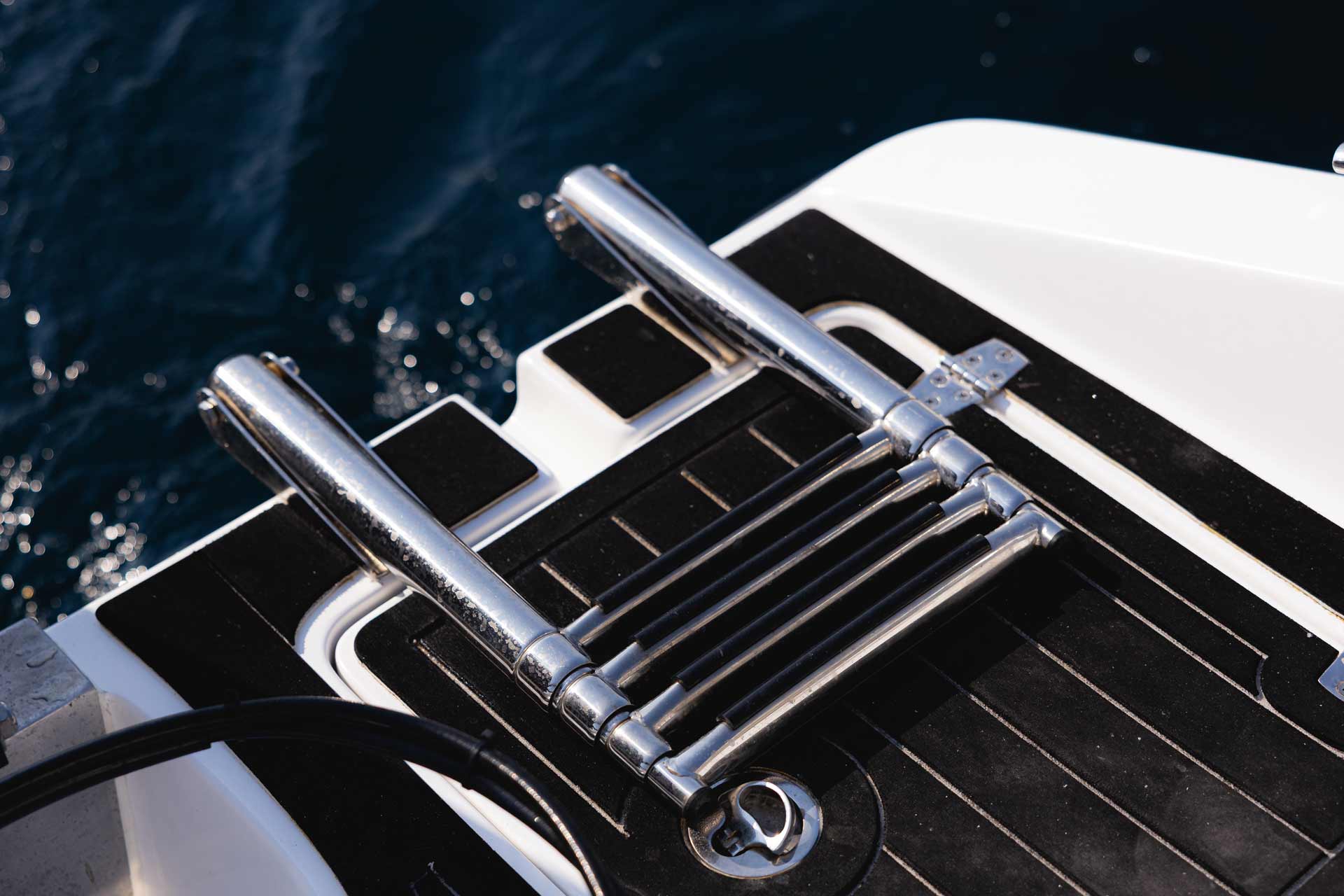 Folded stainless steel boat ladder mounted on a black and white boat deck above dark blue water.