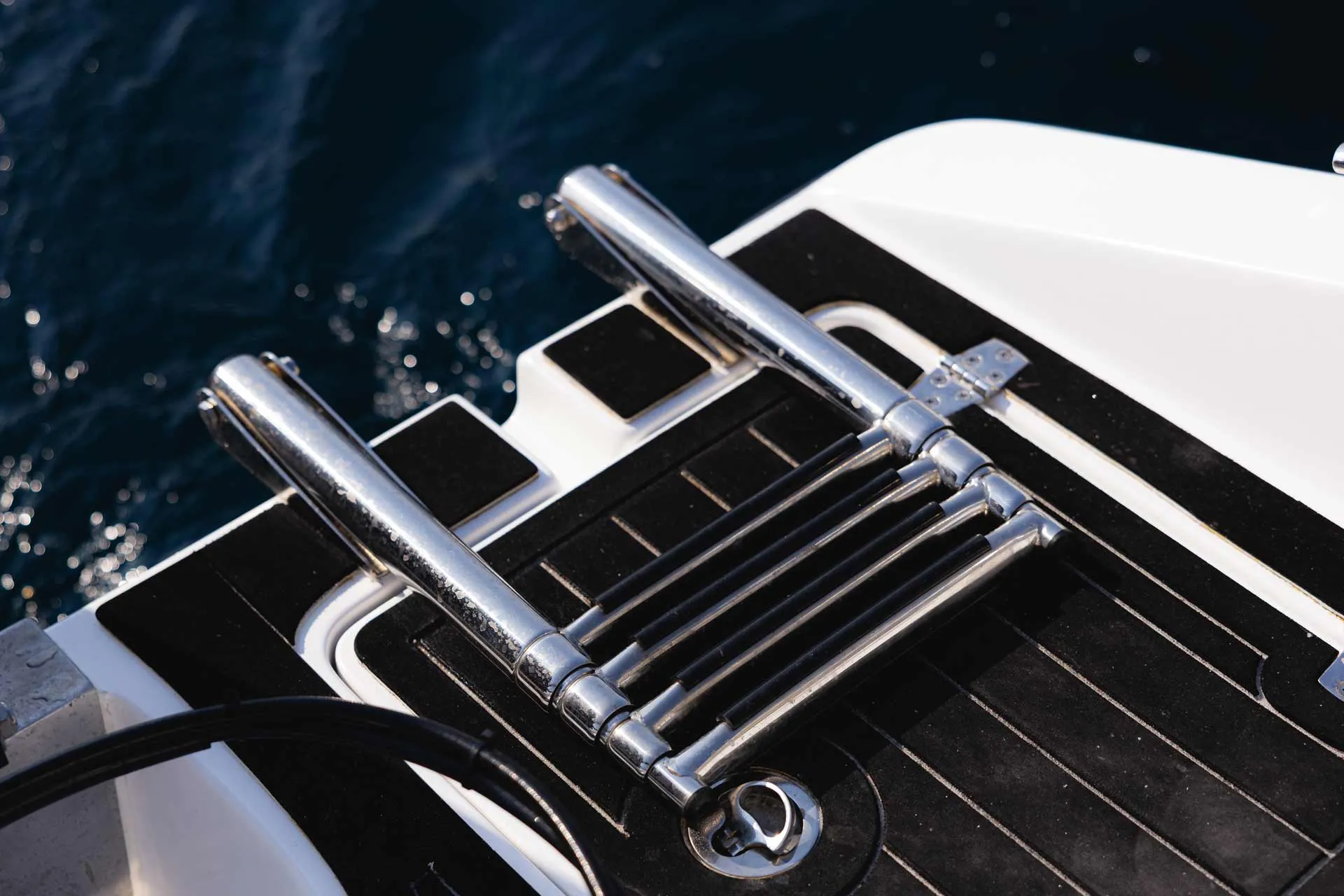 Folded stainless steel boat ladder mounted on a black and white boat deck above dark blue water.