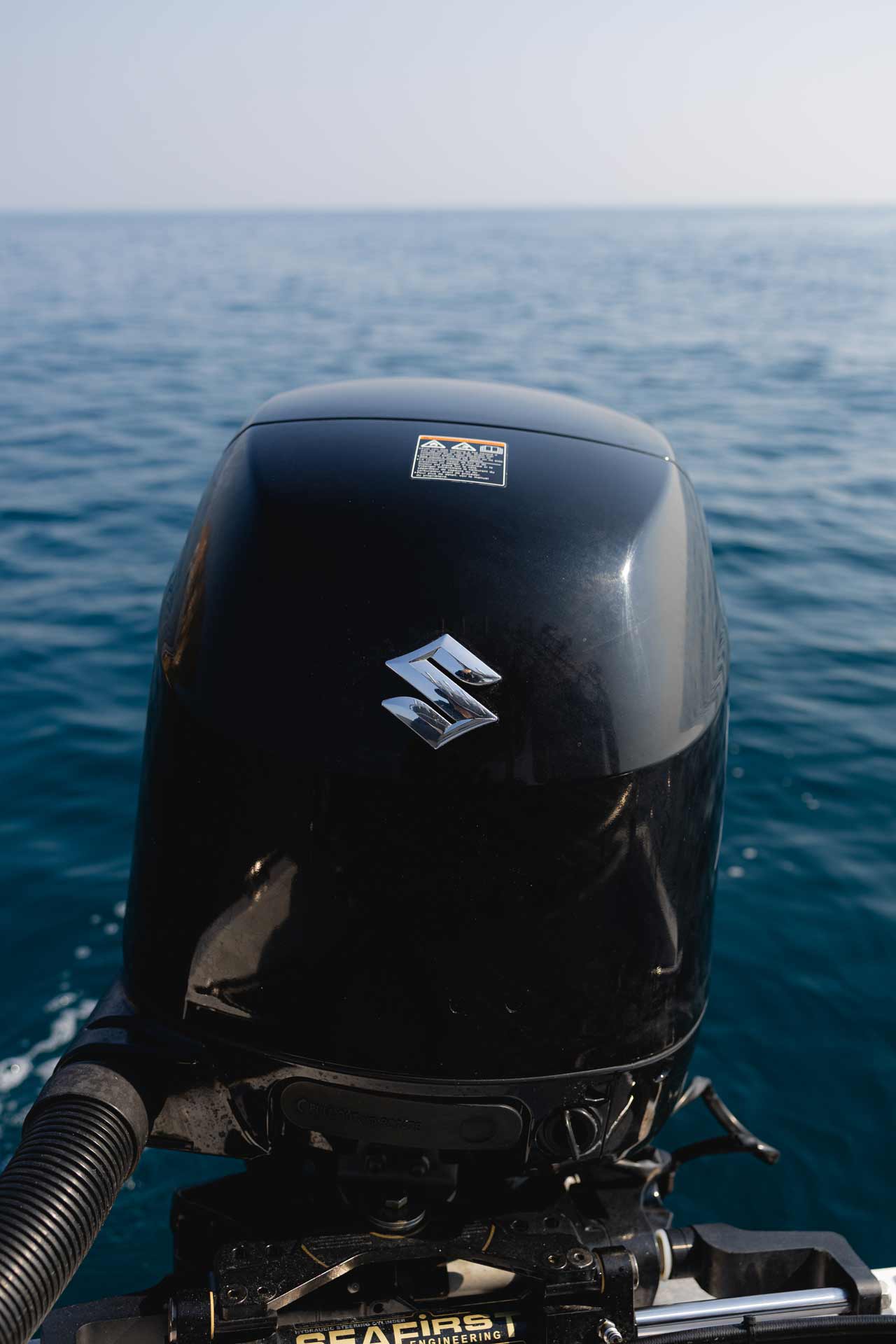Close-up of a black Suzuki boat motor with the sea in the background.