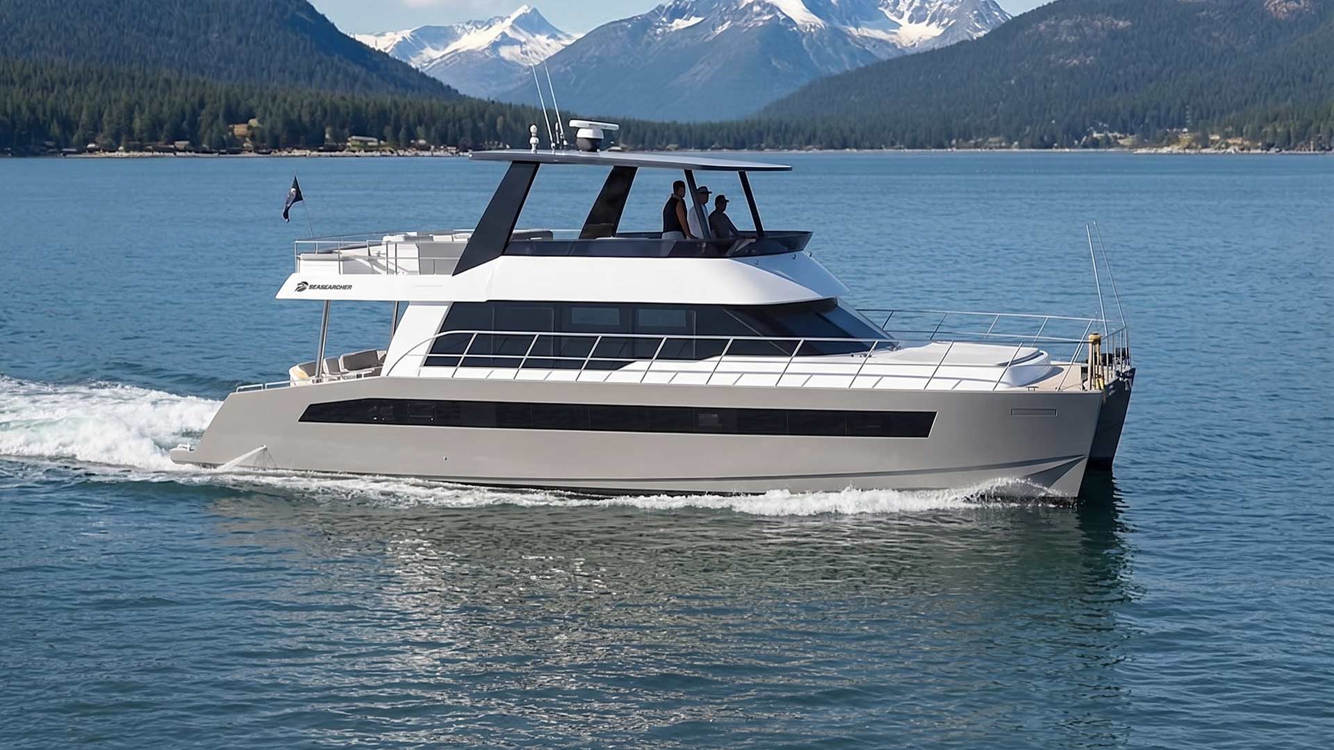 Modern motor yacht cruising on a lake with three people on the upper deck and snowy mountains in the background.