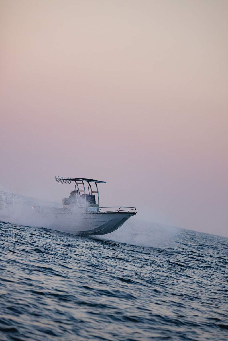Speedboat moving fast on the ocean creating a spray of water at sunset with a clear sky.