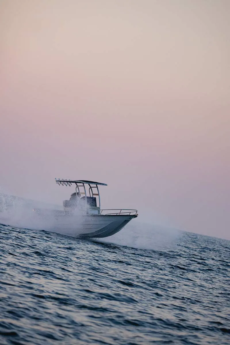 Speedboat moving fast on the ocean creating a spray of water at sunset with a clear sky.
