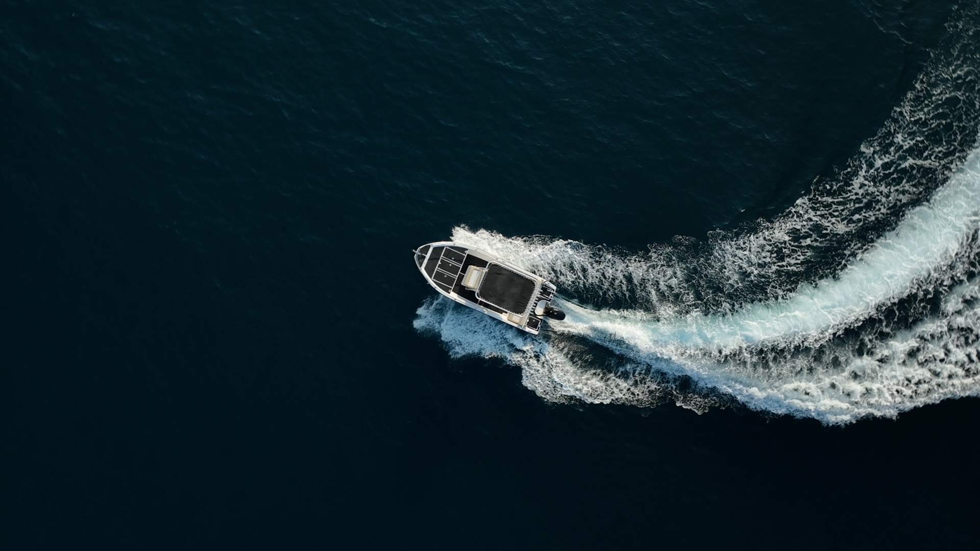 A motorboat making a curved wake on dark blue water, viewed from above.