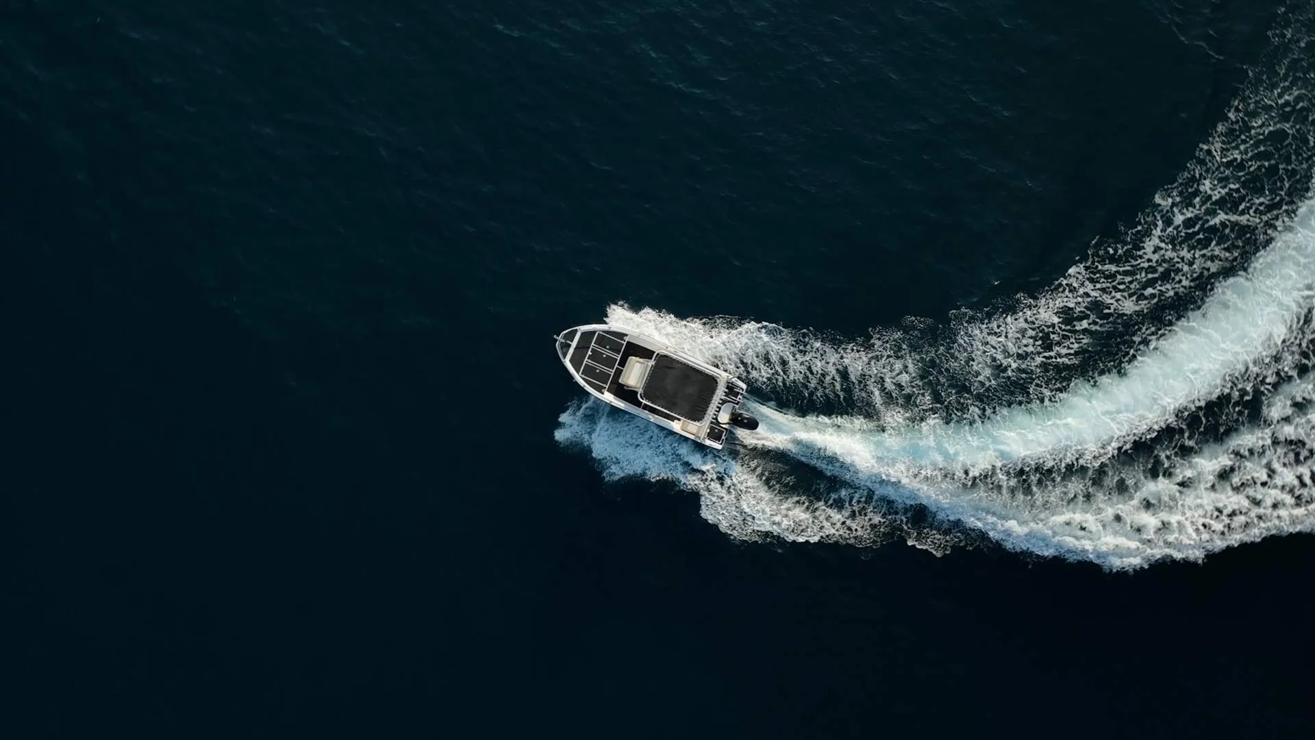 A motorboat making a curved wake on dark blue water, viewed from above.