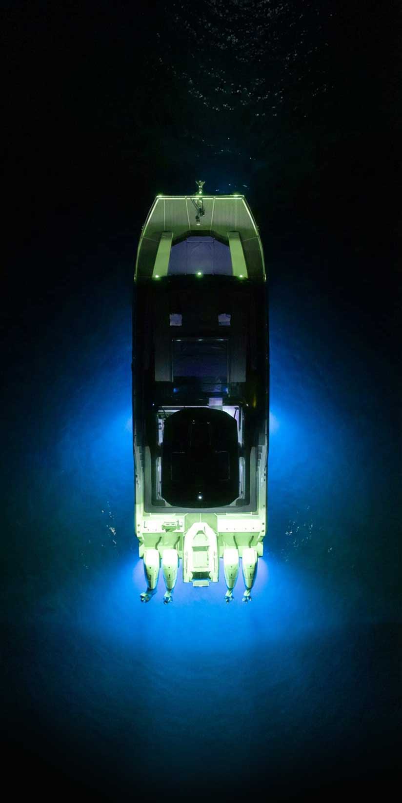 A boat illuminated by blue underwater lights floating on dark water at night, viewed from above.