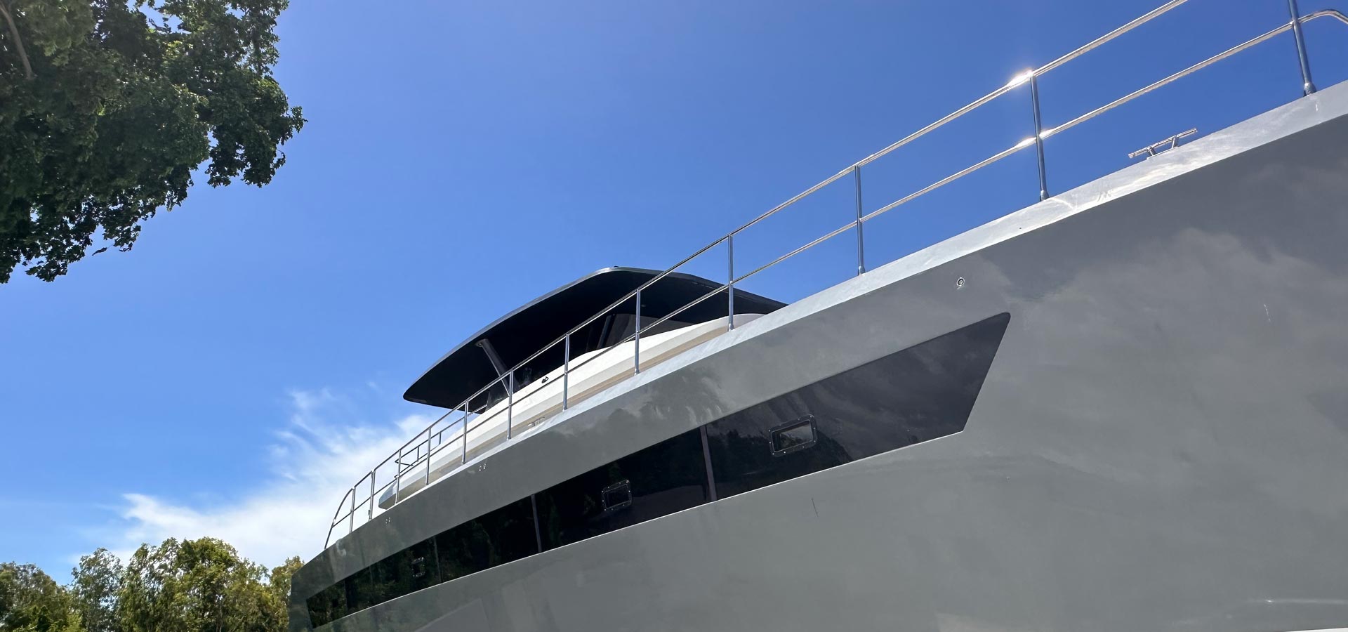 Low angle view of a modern motor yacht under clear blue sky with trees in the background.
