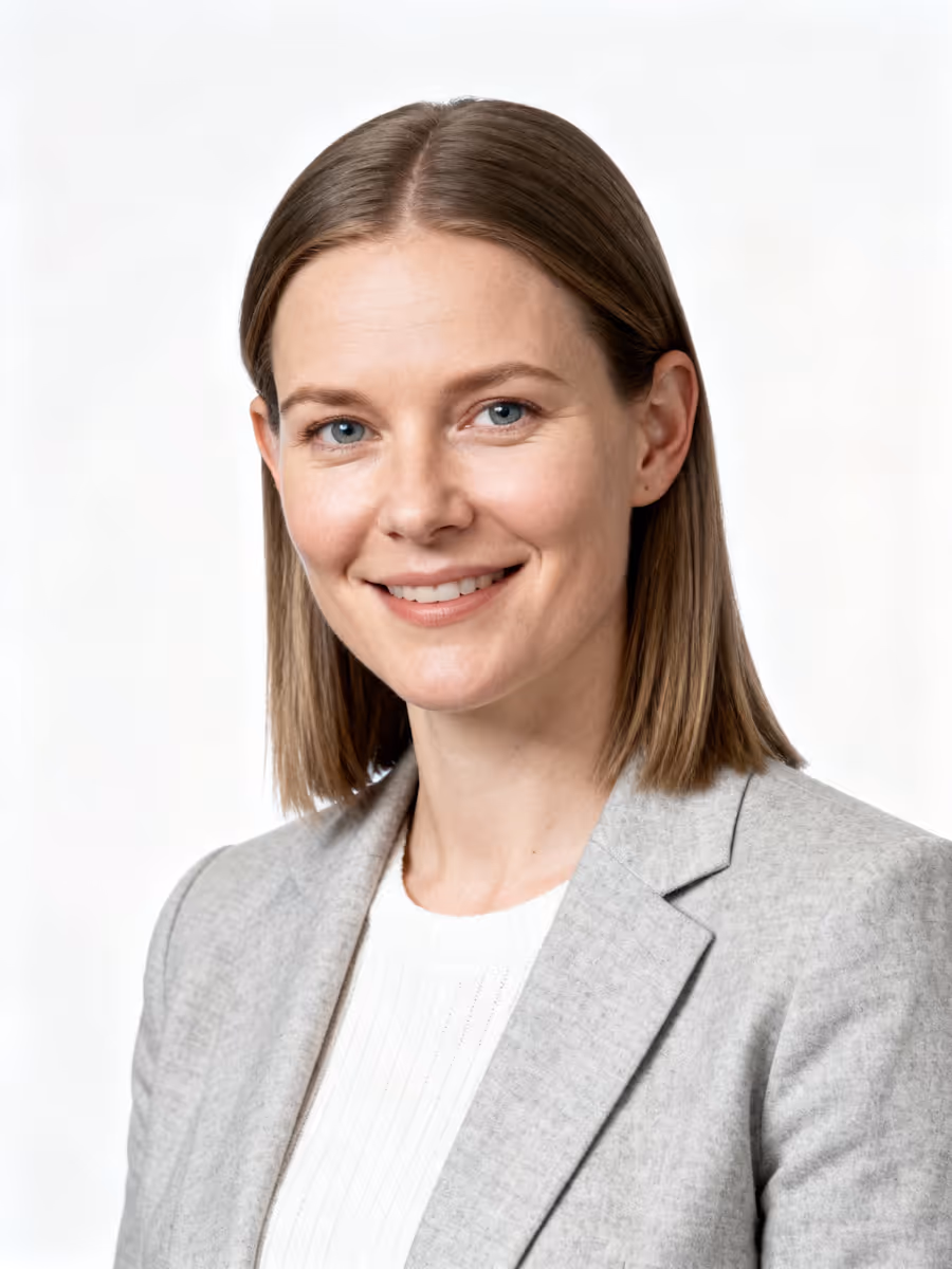 Smiling woman with shoulder-length brown hair wearing a light gray blazer and white top against a white background.