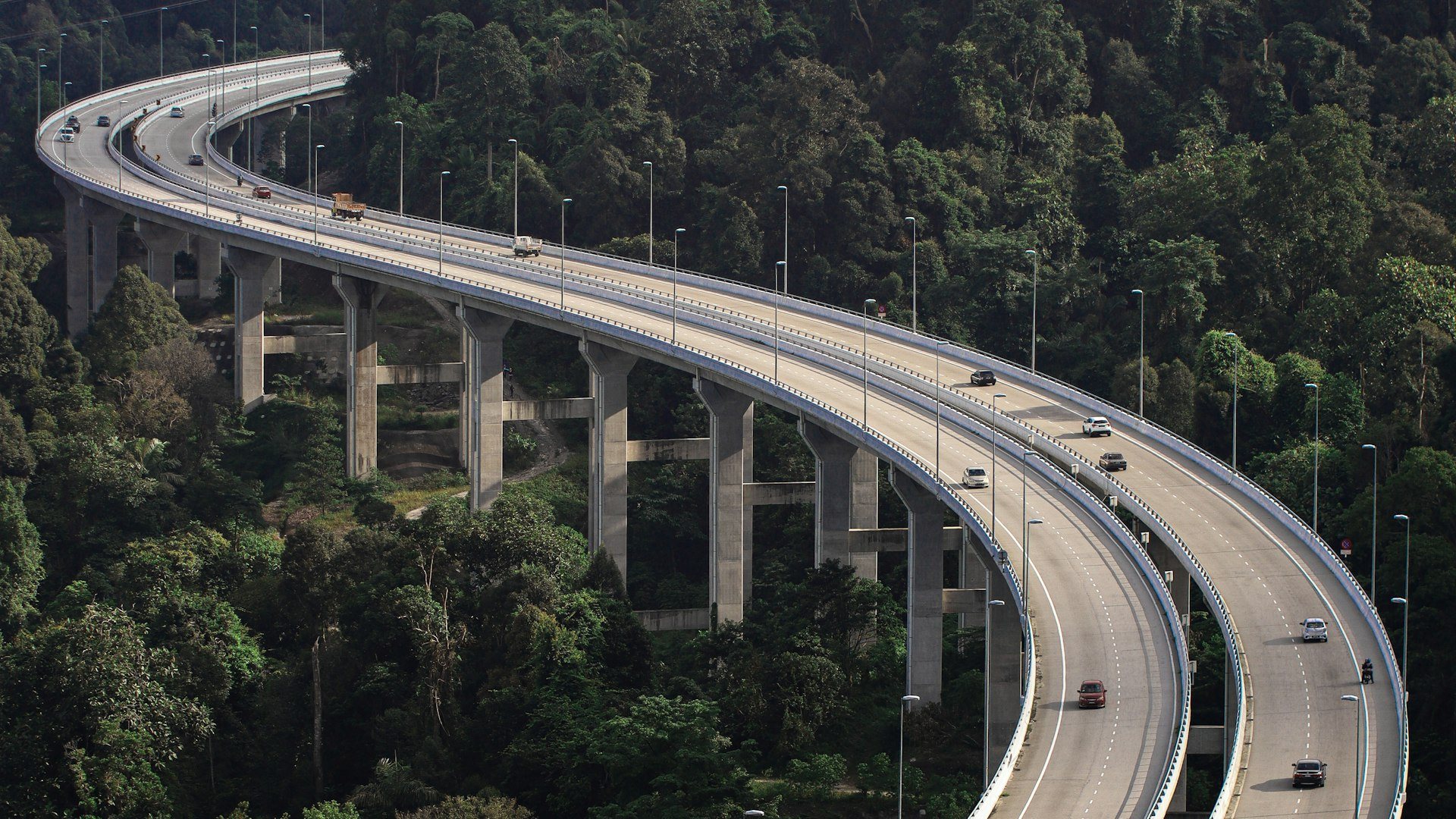 Aerial view of an elevated highway curving through Malaysian rainforest on tall concrete piers