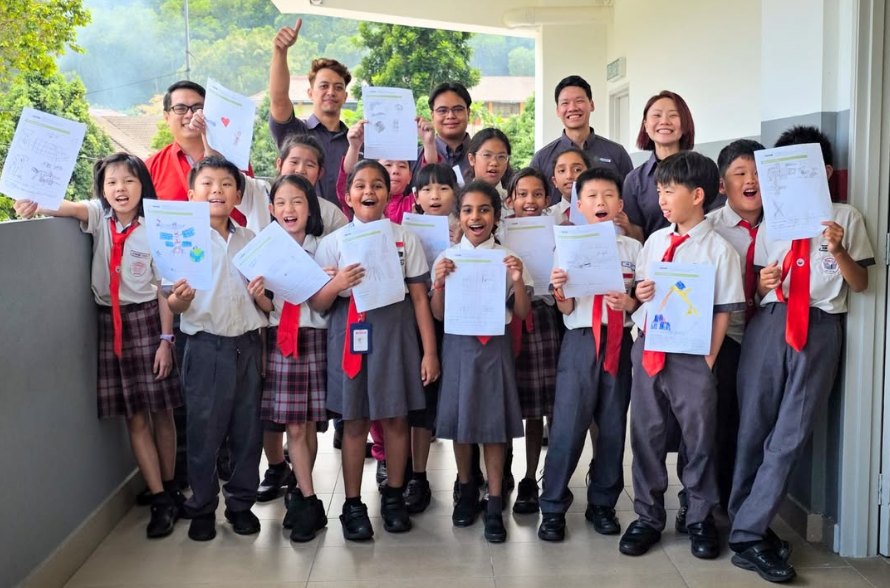 Primary school students holding up completed worksheets, with Protasco staff standing behind them at a school engagement programme.