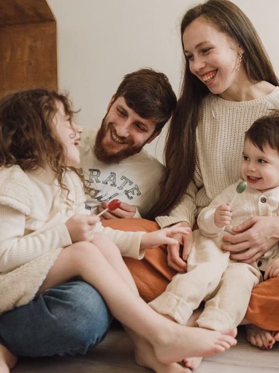 Smiling family with mother, father, and two children sitting close together holding lollipops.