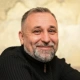 Smiling middle-aged man with salt-and-pepper beard wearing a dark sweater posing indoors.