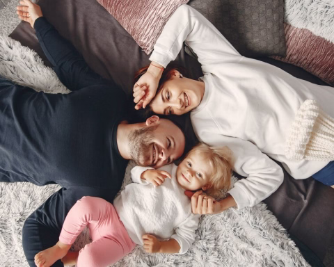 Happy family of two adults and a child lying on soft blankets and pillows smiling.