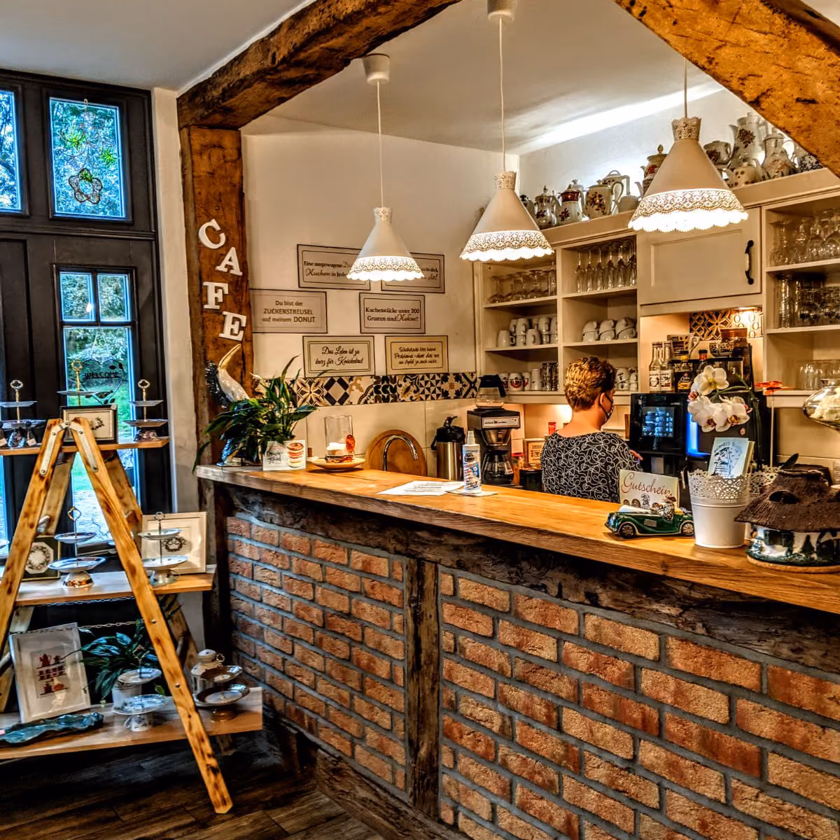 Rustic cafe counter with brick facade, wooden shelves, hanging lamps, and a barista working behind it.