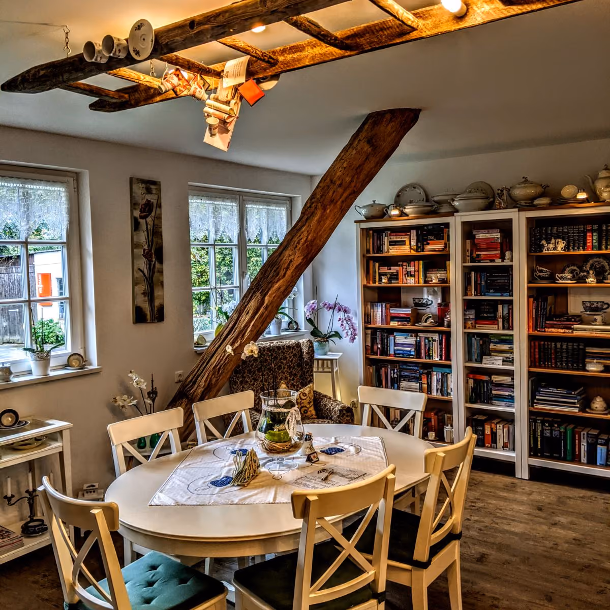 Cozy dining room with a round table, six chairs, wooden bookshelves, and rustic ceiling beam.