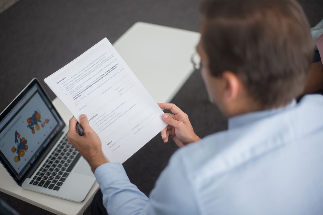 Professional reviewing documents next to a laptop showing charts