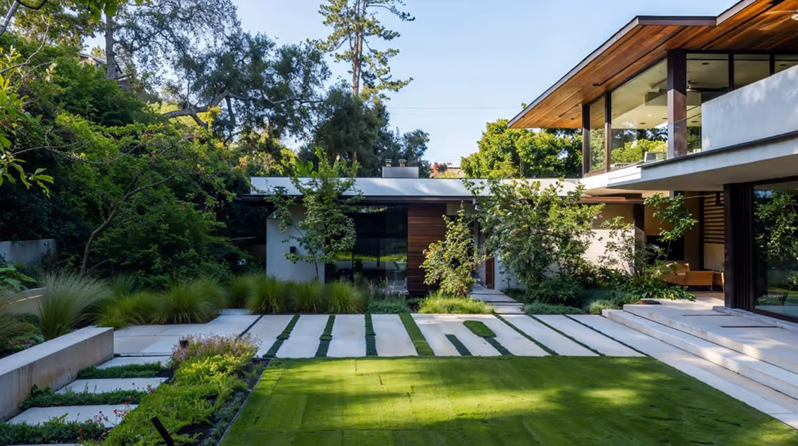 Modern house with large windows, surrounded by lush greenery and a neatly manicured lawn.