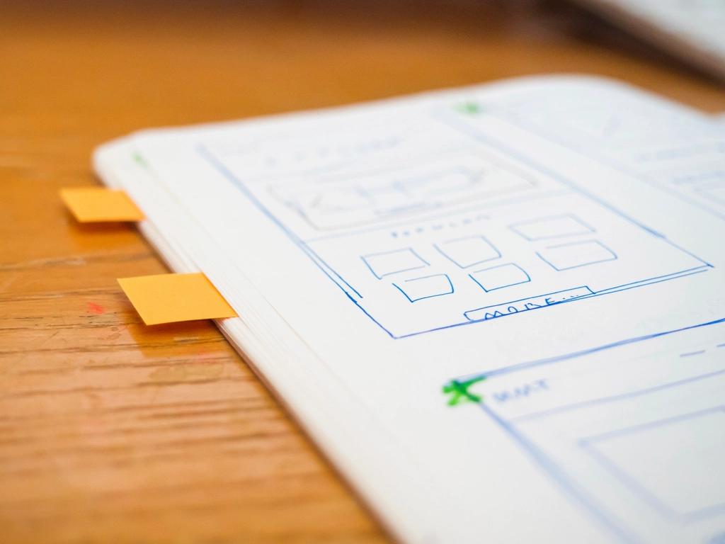 Carnet ouvert sur des wireframes dessines au stylo, deux marque-pages orange sur la tranche.