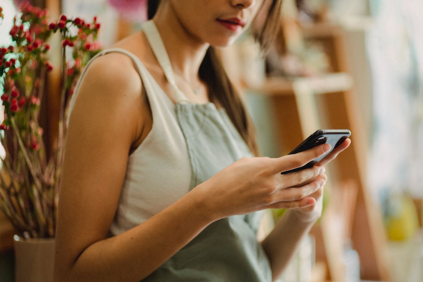 Small shop owner in an apron checking customer messages on her phone