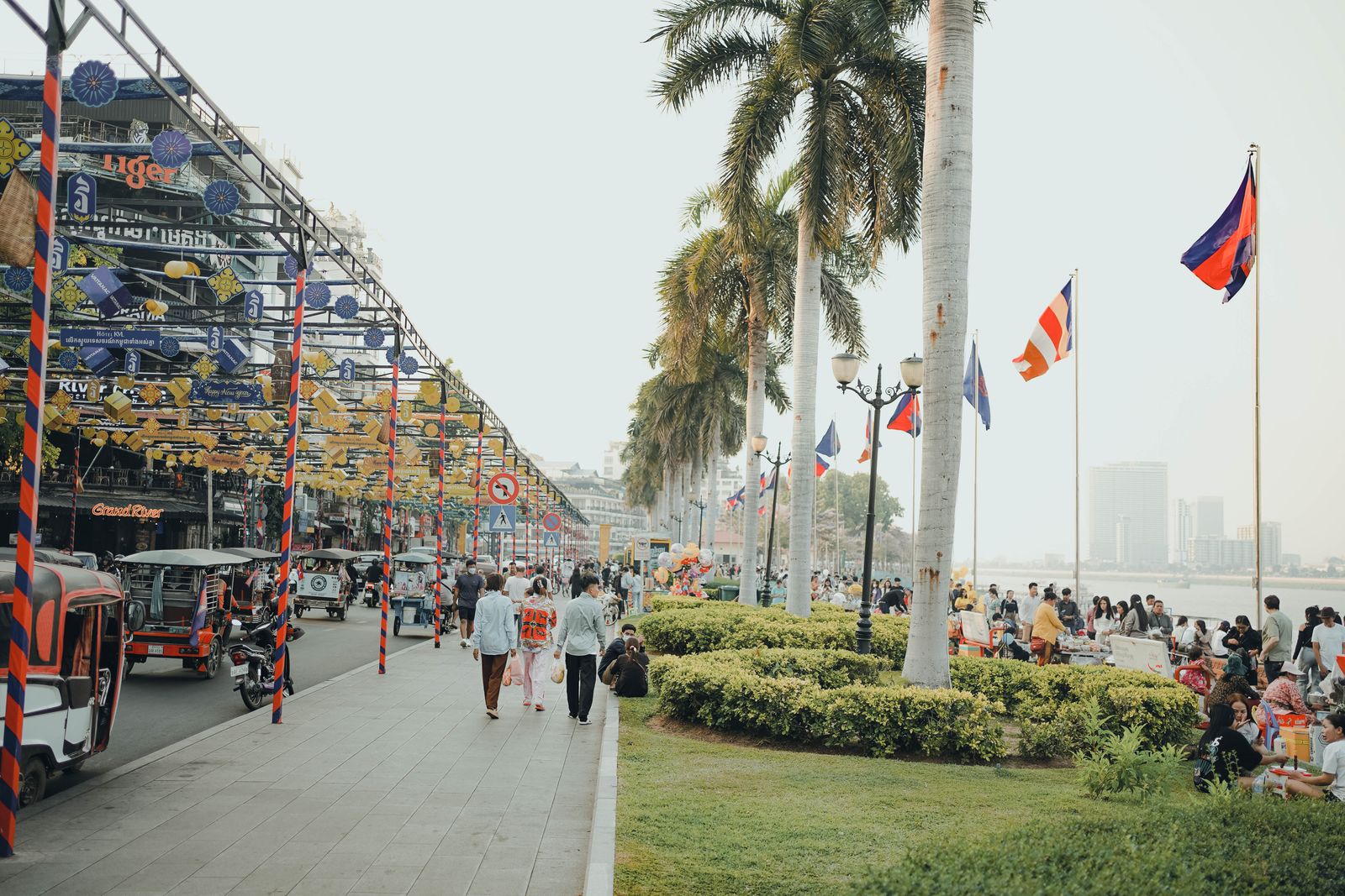 Tuk-tuks and pedestrians on Sisowath Quay, the Phnom Penh riverside, under Cambodian flags