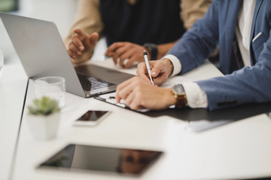 Two people reviewing contract documents beside a laptop on a desk