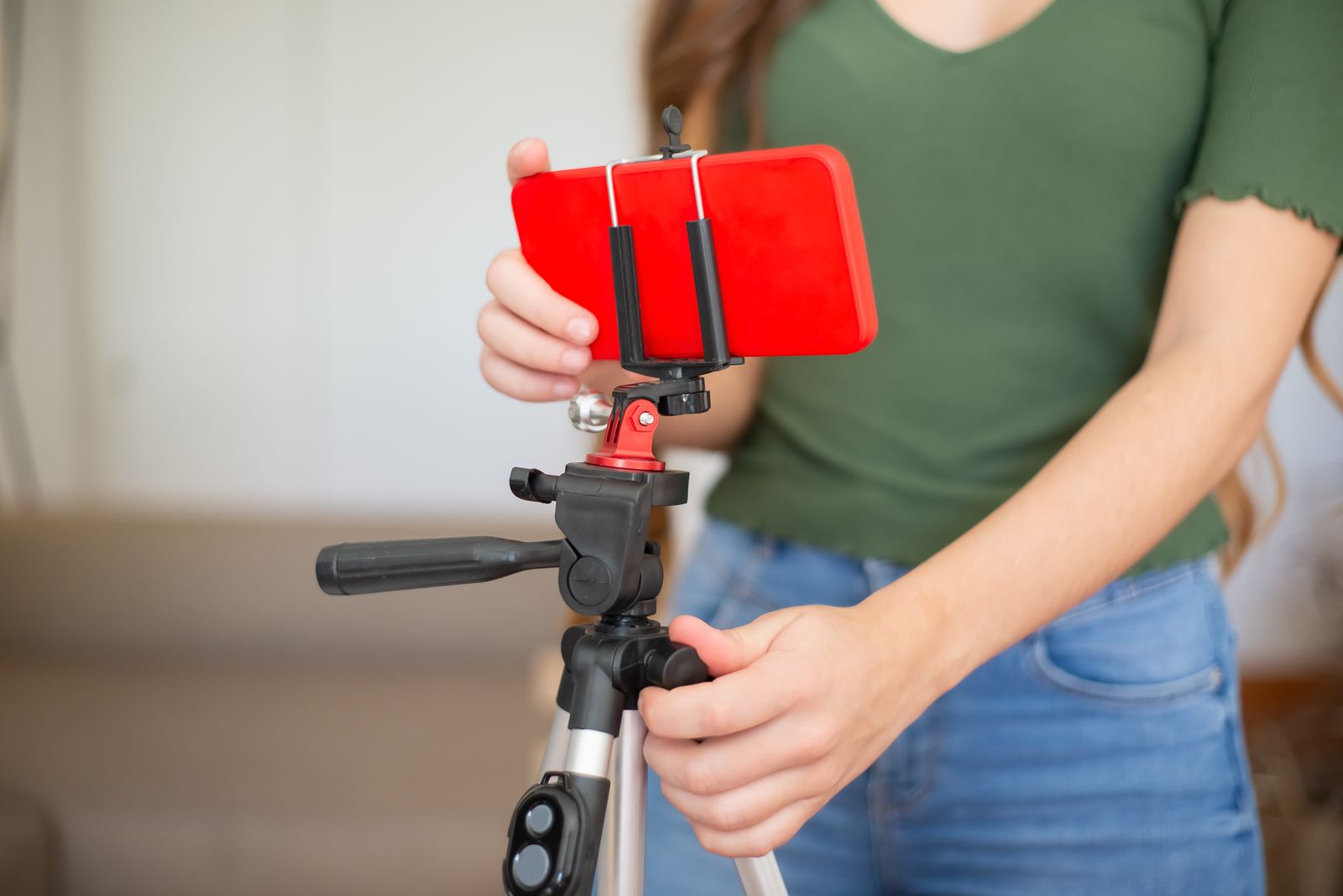 Hands mounting a smartphone in a red case onto a tripod for filming