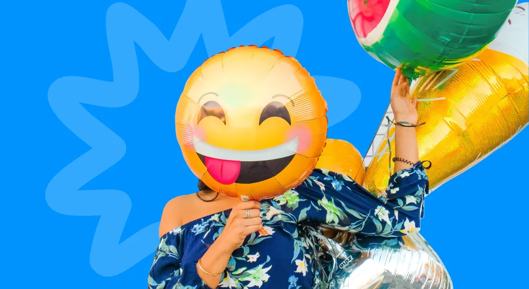 Person holding a smiling emoji foil balloon in front of their face.