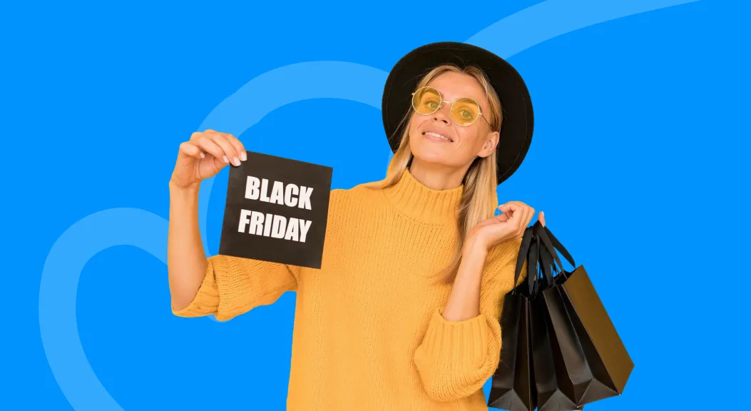 Woman in a yellow jumper and hat holding a Black Friday sign and shopping bags.