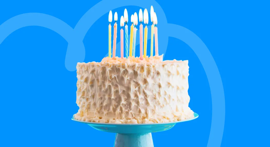 Frosted birthday cake topped with lit candles on a blue cake stand.