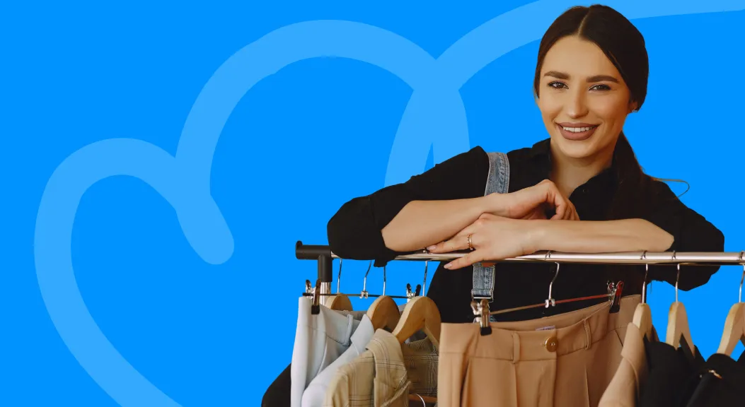 Smiling woman leaning on a clothing rail against a blue background.