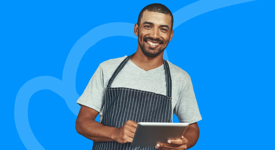 Smiling man in a striped apron holding a tablet.