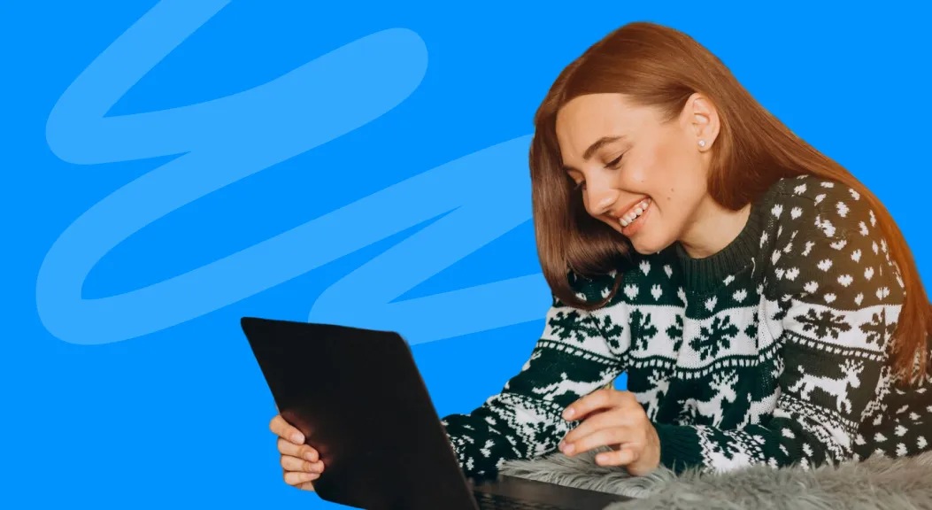 Woman in a Christmas jumper smiling at a tablet.