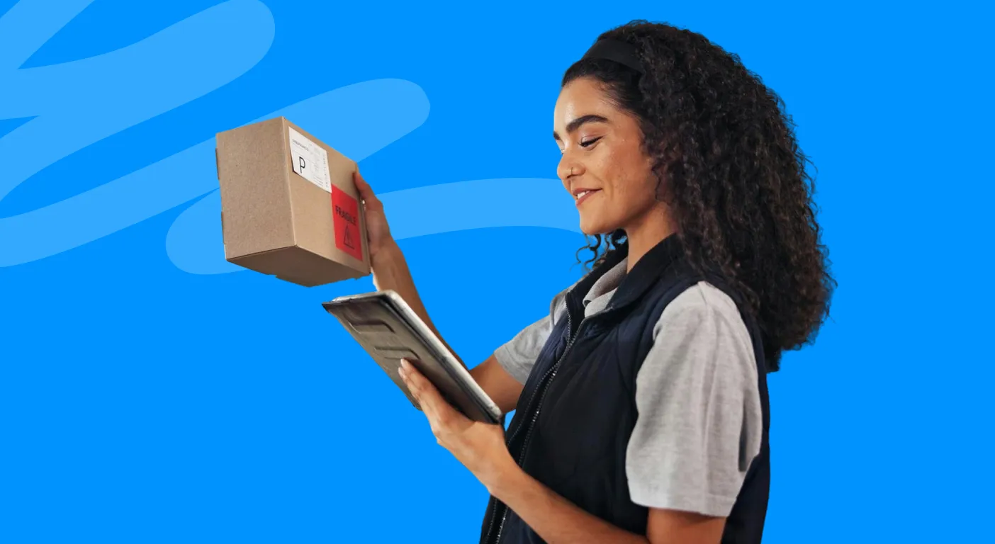 Warehouse worker checking a tablet while holding a cardboard box.