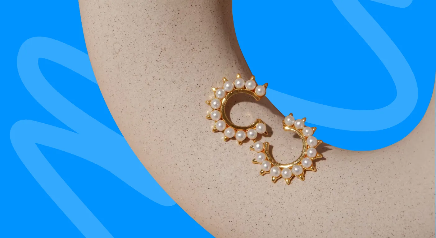 Gold and pearl hoop earring displayed on a sand-coloured stand.