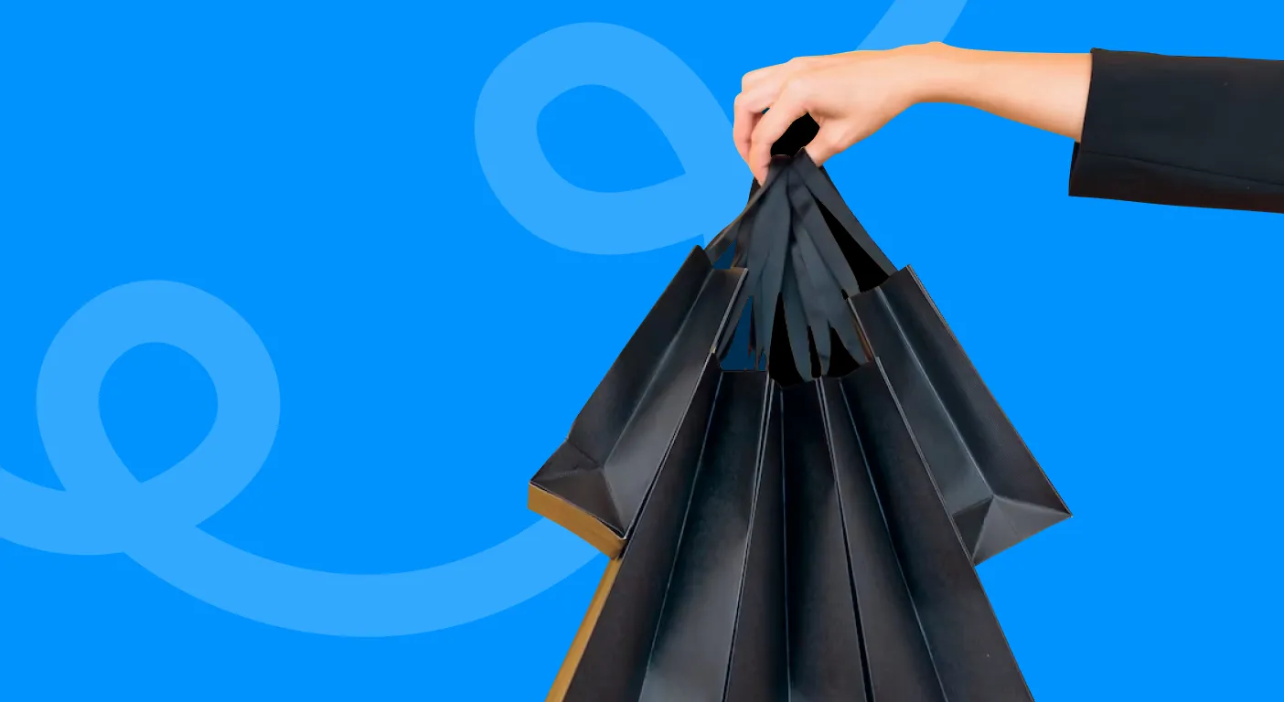 Hand holding a bundle of black paper shopping bags.