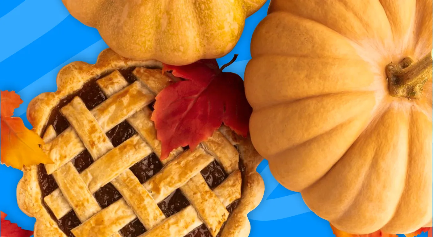 Lattice-topped pie beside pumpkins and red autumn leaves.