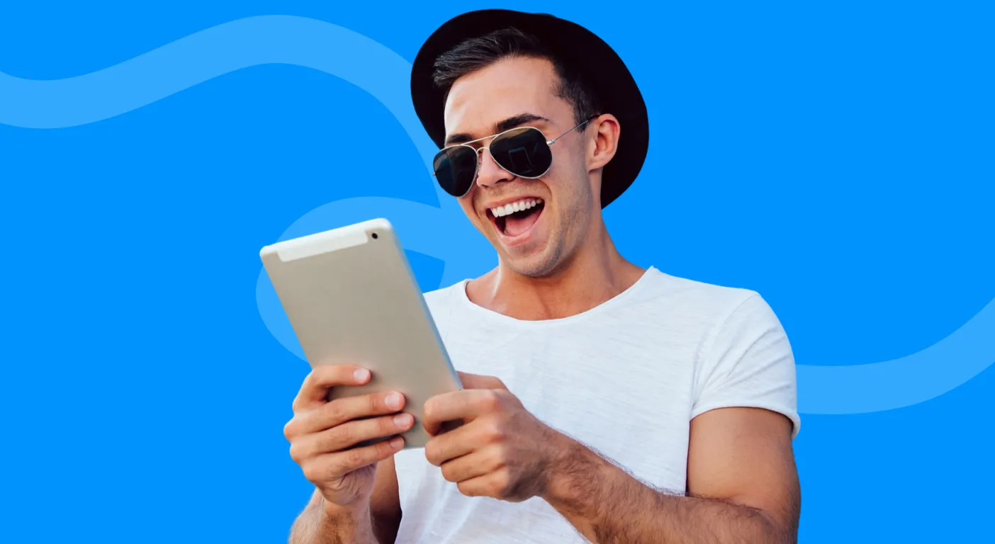 Man in sunglasses and a black hat laughing at a tablet screen.