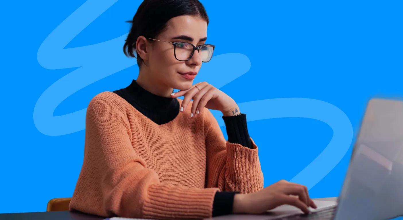 Woman in glasses and an orange jumper reading on a laptop against a blue background.