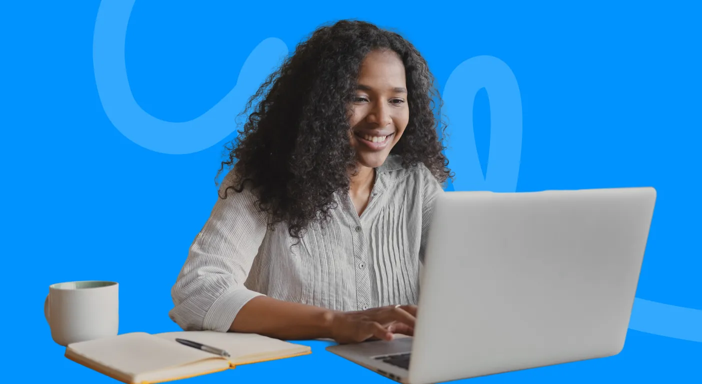 Smiling woman typing on a laptop beside a notebook and a mug of coffee.