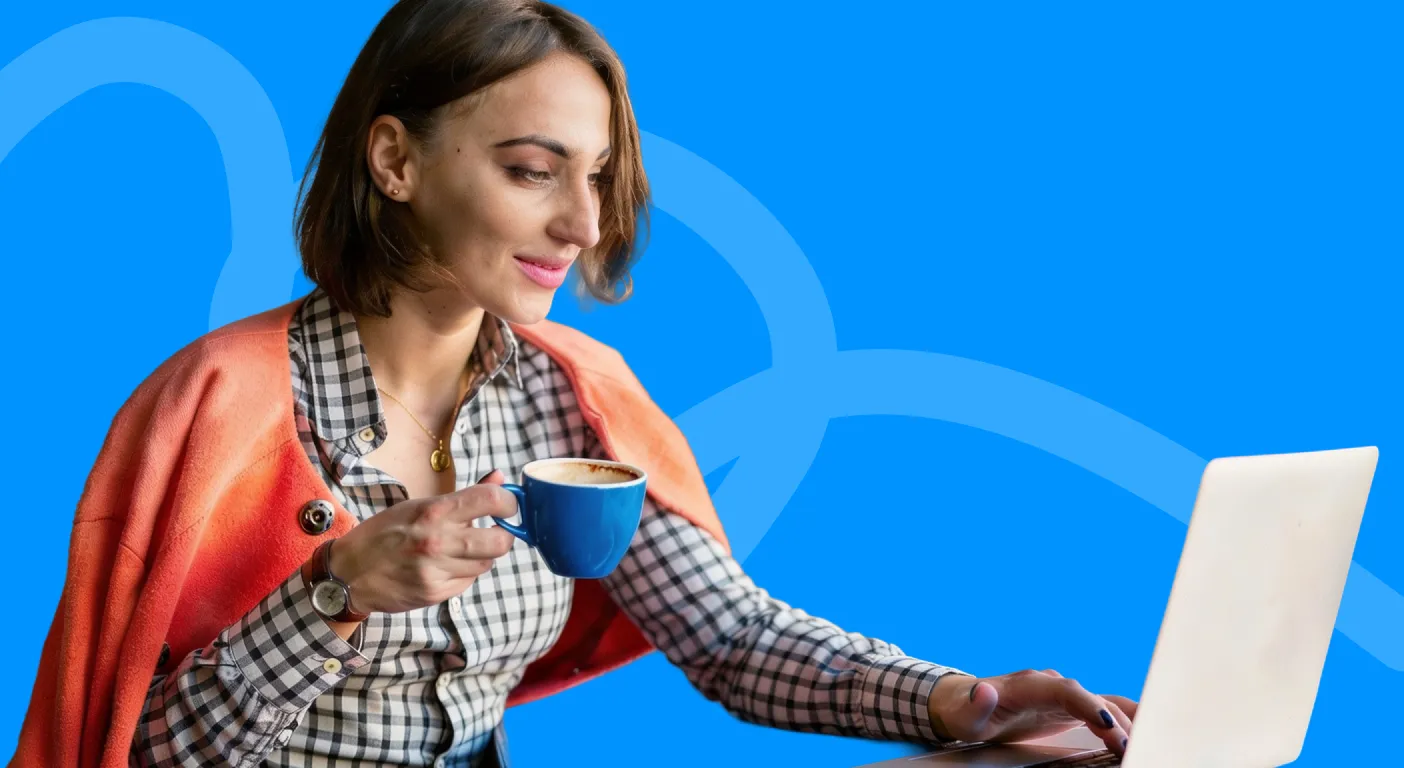 Woman holding a cup of coffee while reading on her laptop.