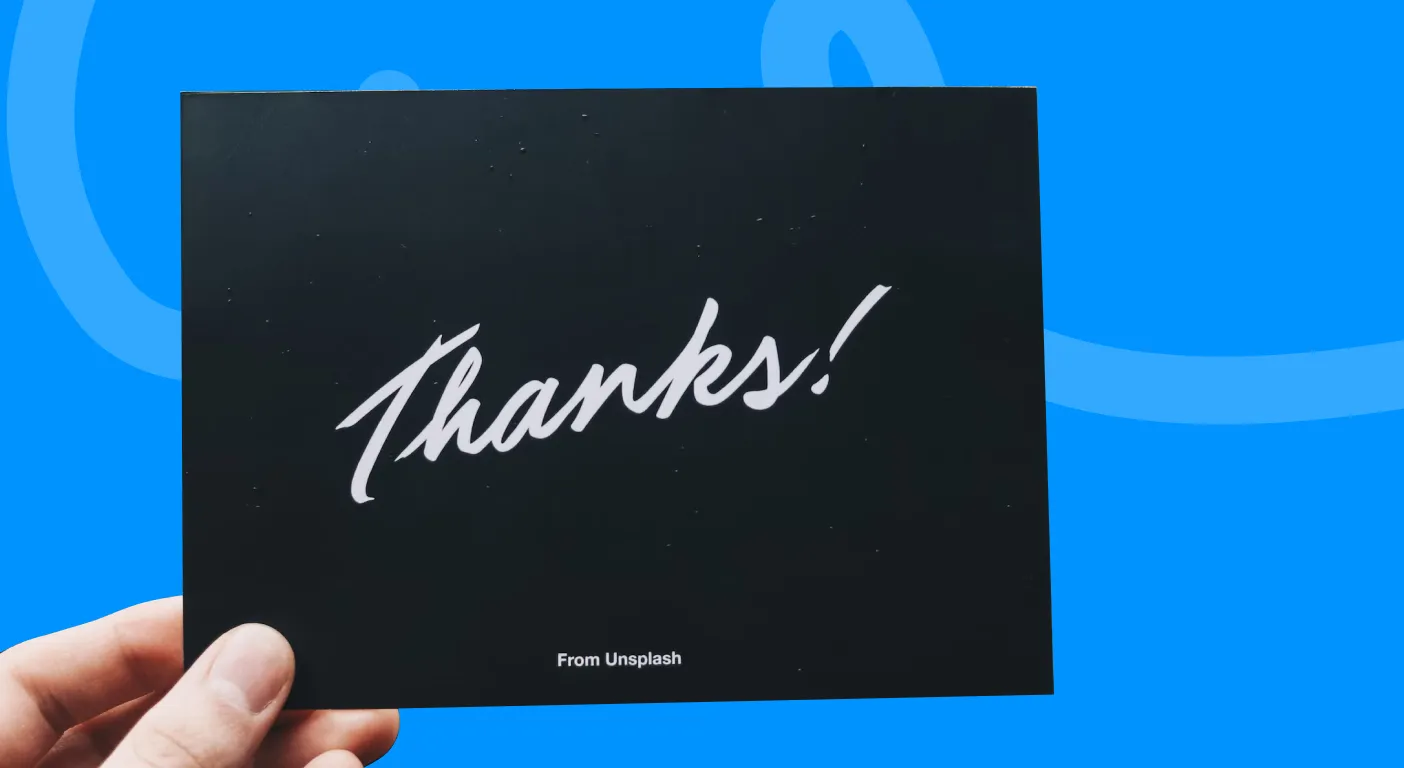 Hand holding a black card with Thanks written in white script.