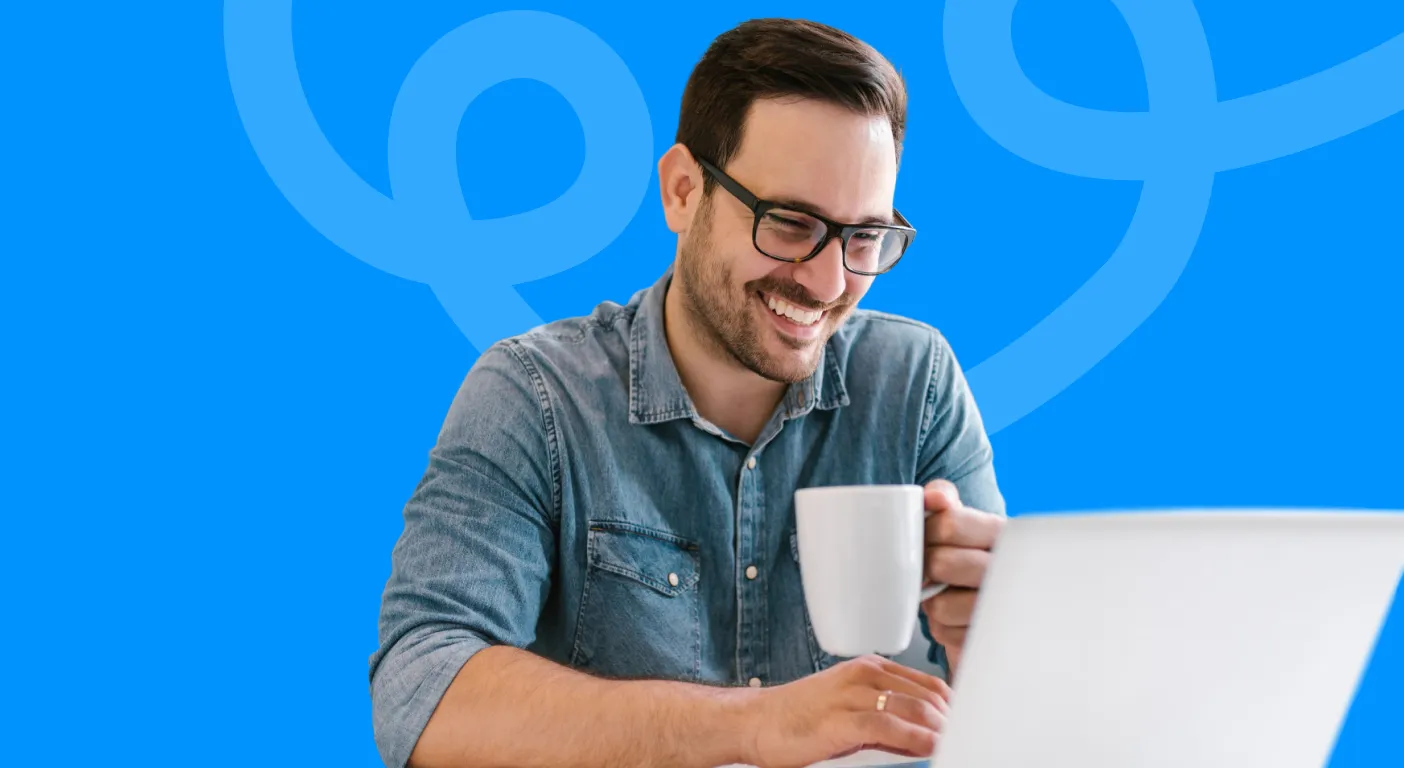 Smiling man in glasses reading his laptop while holding a mug.